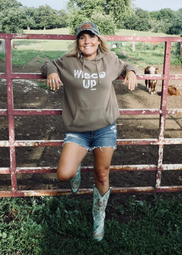 Woman in a hoodie with 'Wesco Up' text, standing next to a metal gate with cows in the background.