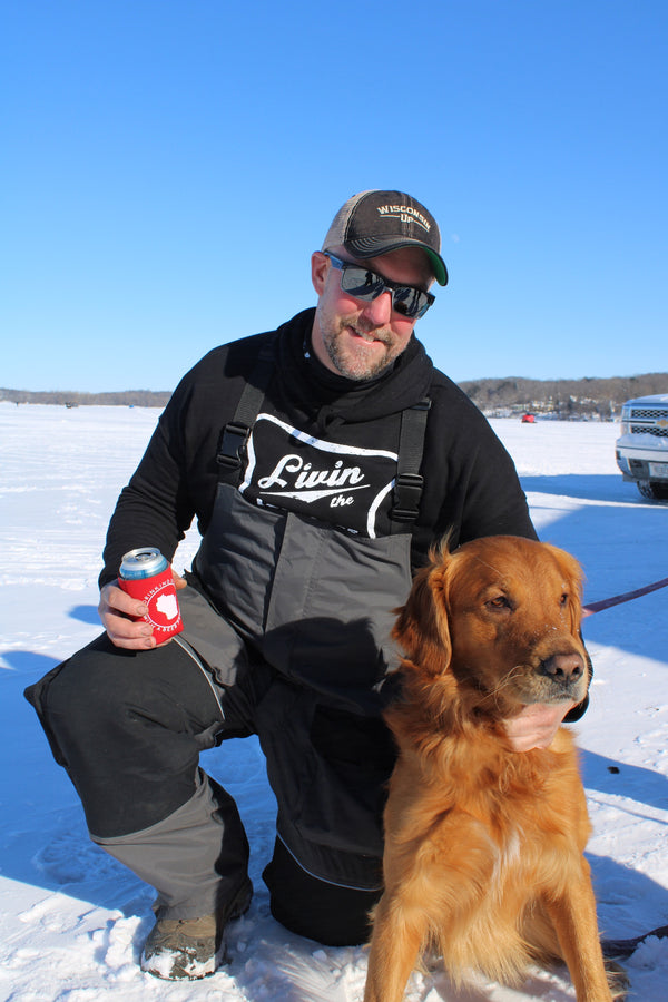 "Livin' the Ice Life" hoodie for winter enthusiasts, perfect for staying warm during cold-weather activities. On a male model who is ice fishing with his dog.