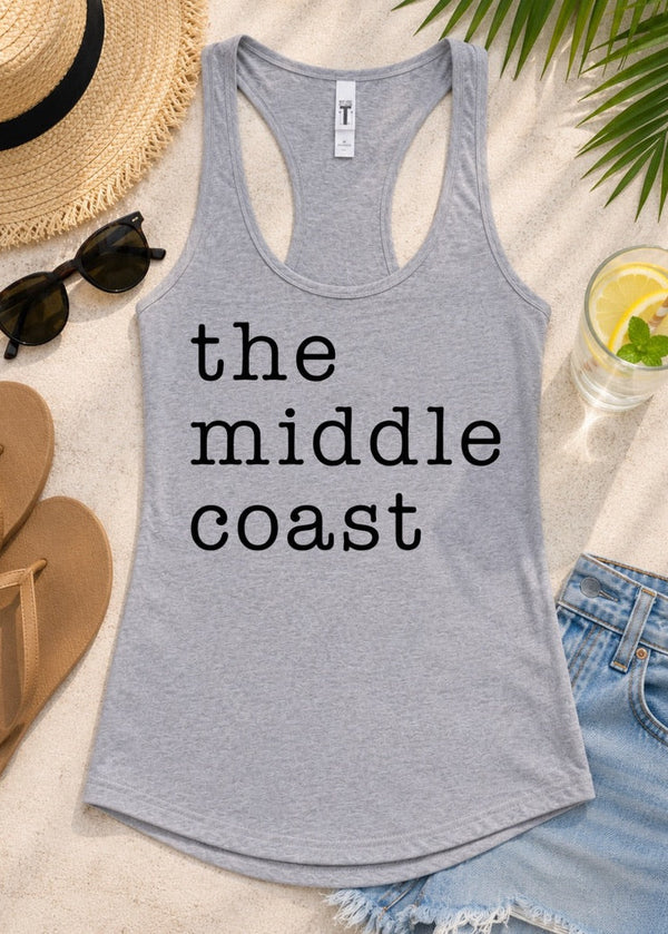 A heather gray racerback tank top with the text 'the middle coast' printed in black lowercase letters, styled in a beach-themed flat lay with sunglasses, a straw hat, sandals, denim shorts, and a drink on a light sandy background.