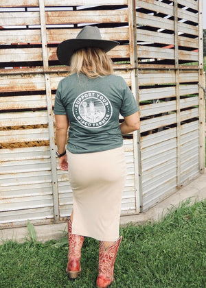 Person wearing a green t-shirt with a logo and text, standing in front of a wooden fence.