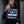 Load image into Gallery viewer, Person wearing a hoodie with text, holding a drink against a wooden background
