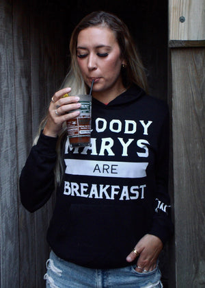 Person wearing a hoodie with text, holding a drink against a wooden background