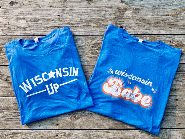 Two blue t-shirts with 'Wisconsin' text on a wooden surface