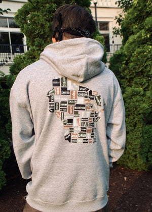 Person wearing a gray hoodie with a patterned back design of Wisconsin counties outdoors.