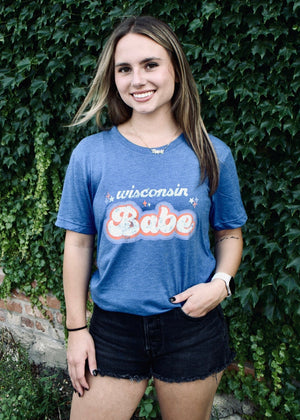 Woman wearing a blue t-shirt with 'Wisconsin Babe' text against a green ivy wall.