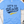Load image into Gallery viewer, A light blue crewneck t-shirt with a distressed graphic reading 'LET'S GO Wisco' in navy and yellow, laid flat on a light wood background with baseball-themed props.
