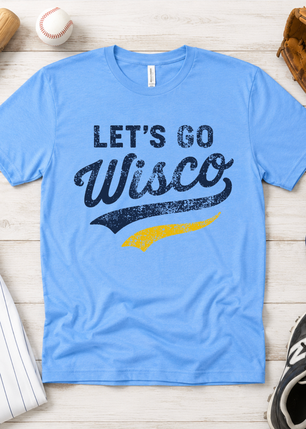 A light blue crewneck t-shirt with a distressed graphic reading 'LET'S GO Wisco' in navy and yellow, laid flat on a light wood background with baseball-themed props.