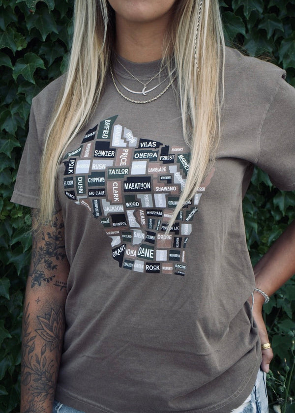 Person wearing a brown t-shirt with graphic design against a green leafy background
