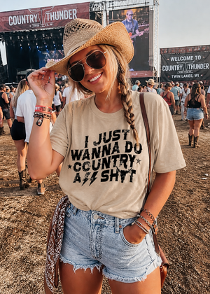 Woman at a music festival wearing a t-shirt with text, denim shorts, and a straw hat.