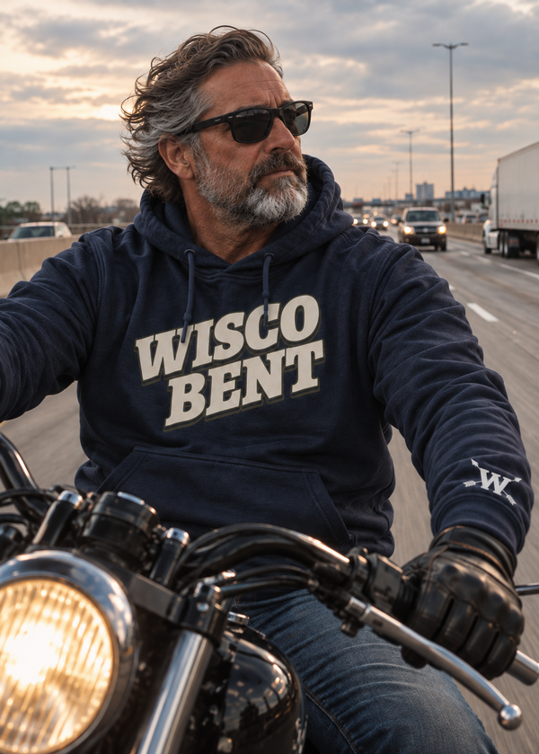 A man with a graying beard and sunglasses rides a motorcycle on a highway, wearing a navy blue hoodie with 'WISCO BENT' printed in white across the chest.