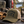 Load image into Gallery viewer, An olive green trucker hat with 'WISCONSIN UP OUTFITTERS' embroidered on the front, resting on the tailgate of a pickup truck outdoors near a lake and pine trees. A plaid blanket, leather gloves, a cooler, and a travel mug are also visible in the scene.
