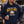 Load image into Gallery viewer, A man wearing a navy blue hoodie with a 'Now That's The Wisco Way 2025 Champions' graphic, standing outdoors at a tailgate or barbecue event and holding a beer can.
