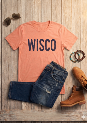 Coral t-shirt with 'WISCO' text, blue jeans, brown boots, and sunglasses on a wooden surface.