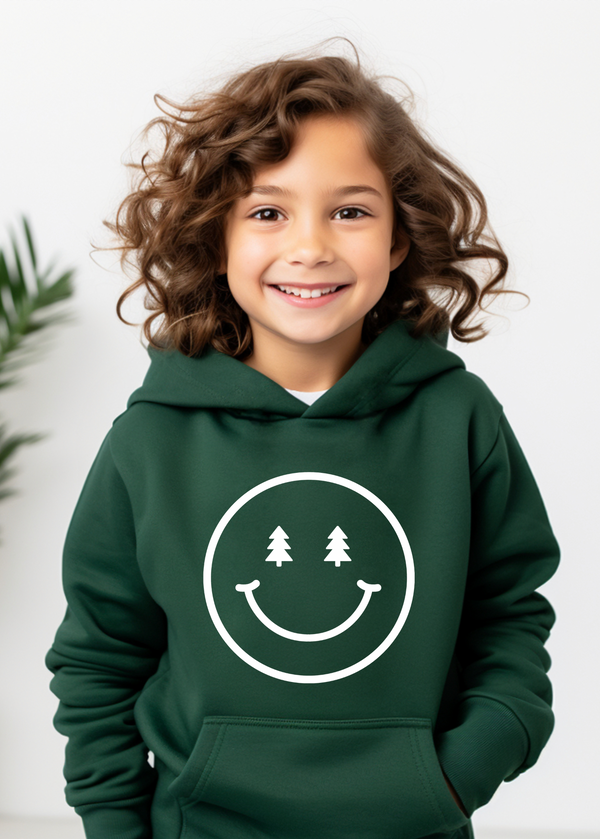 Child wearing a green hoodie with a smiley face design featuring trees, standing indoors.