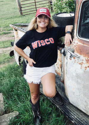 Woman in a 'Wisco' shirt leaning against an old truck in a rural setting