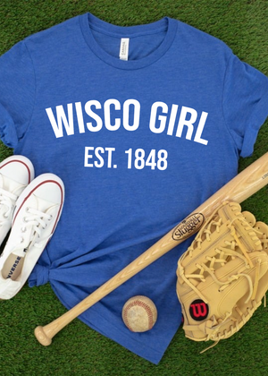 Blue t-shirt with 'WISCO GIRL EST. 1848' text, white sneakers, baseball bat, and glove on grass.