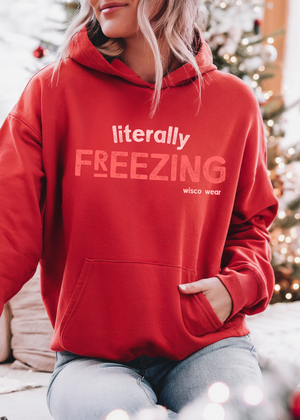 Person wearing a red hoodie with 'literally FREEZING' text in a festive indoor setting.