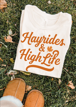 White t-shirt with 'Hayrides & High Life' text on grass with brown shoes
