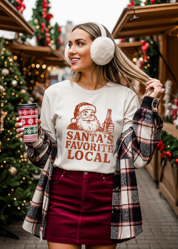 Woman in festive outfit with 'Santa's Favorite Local' shirt at a Christmas market.